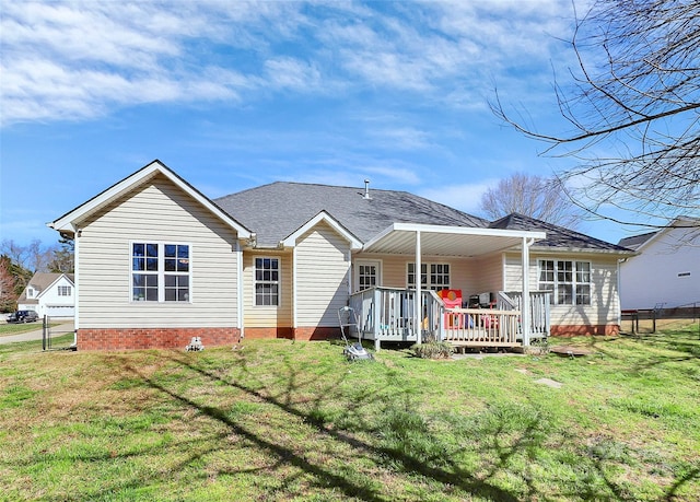 rear view of property featuring a wooden deck, a lawn, and roof with shingles