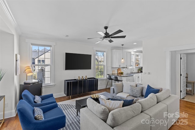 living area featuring ceiling fan, baseboards, ornamental molding, and light wood finished floors