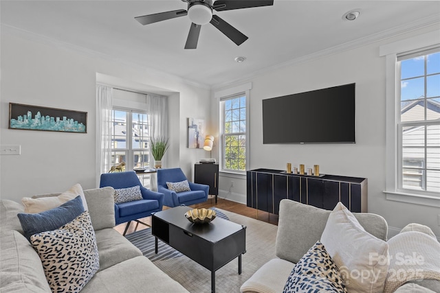 living area featuring wood finished floors, a healthy amount of sunlight, baseboards, and ornamental molding