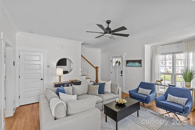 living room featuring stairway, crown molding, light wood-type flooring, and a ceiling fan