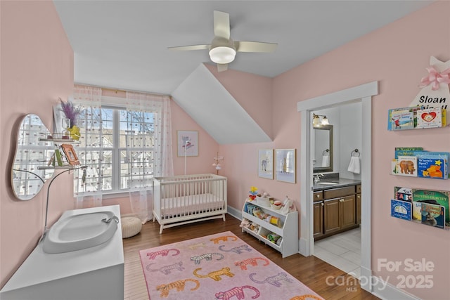 bedroom with a sink, a nursery area, wood finished floors, and ensuite bathroom