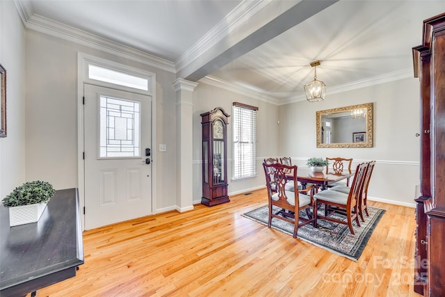 dining room featuring light wood finished floors, crown molding, and decorative columns