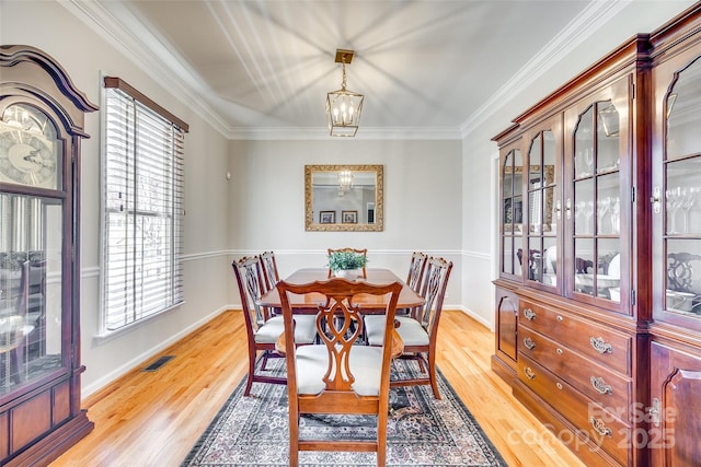 dining area featuring visible vents, light wood-style floors, an inviting chandelier, and ornamental molding