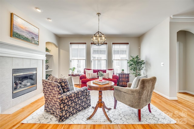 living area with baseboards, a tile fireplace, wood finished floors, arched walkways, and a notable chandelier