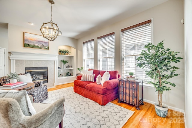 living area with built in shelves, baseboards, a tile fireplace, an inviting chandelier, and wood finished floors