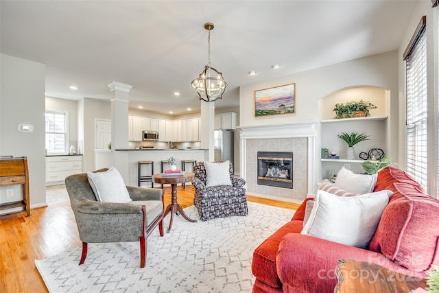 living area featuring a chandelier, recessed lighting, a fireplace, light wood-style floors, and ornate columns