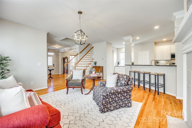 living area featuring stairs, decorative columns, light wood-type flooring, and a wealth of natural light