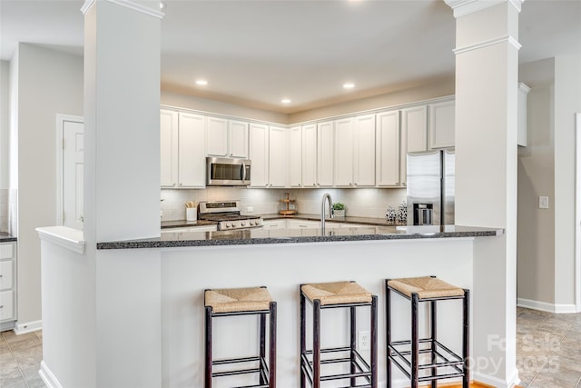 kitchen with ornate columns, dark stone counters, stainless steel appliances, a kitchen bar, and tasteful backsplash