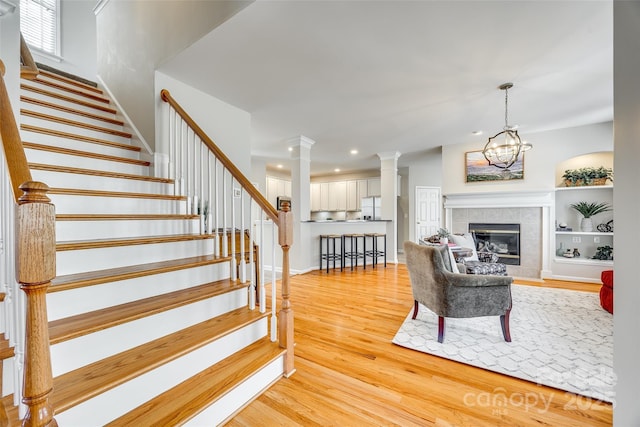 living area featuring recessed lighting, light wood-style floors, a fireplace, decorative columns, and stairs