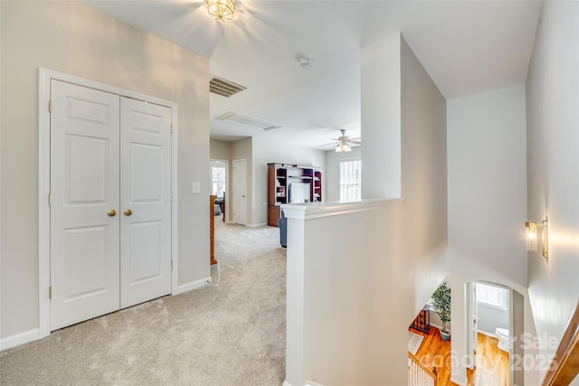 hallway featuring visible vents, an upstairs landing, baseboards, light colored carpet, and attic access