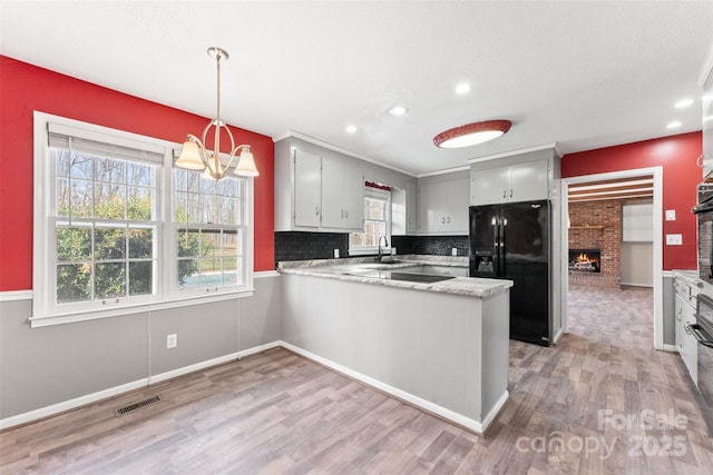 kitchen with visible vents, a peninsula, light wood-style flooring, black appliances, and a chandelier