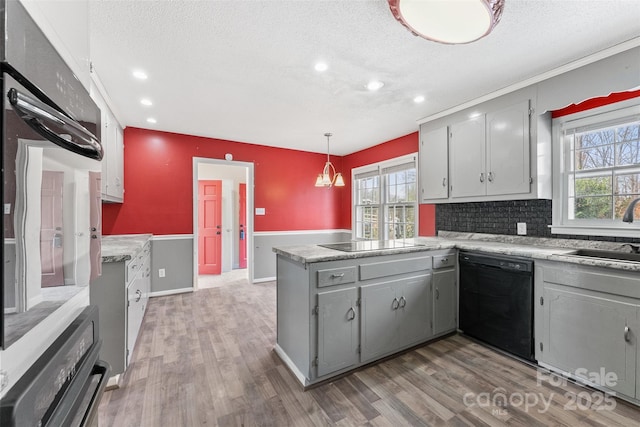 kitchen with black appliances, gray cabinets, a sink, wood finished floors, and a peninsula