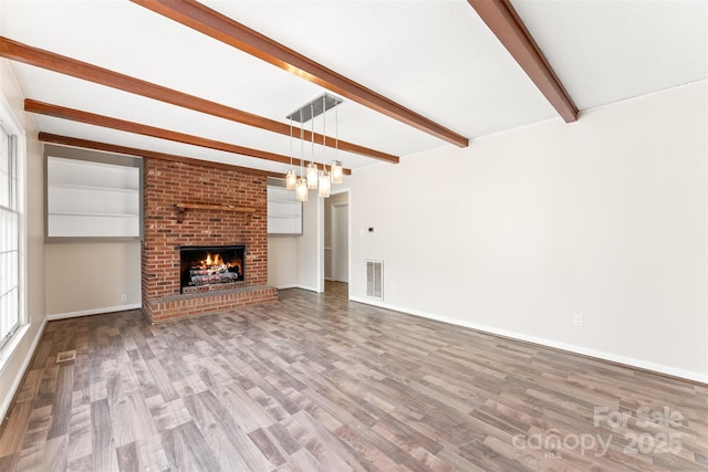 unfurnished living room with visible vents, beamed ceiling, a brick fireplace, and wood finished floors