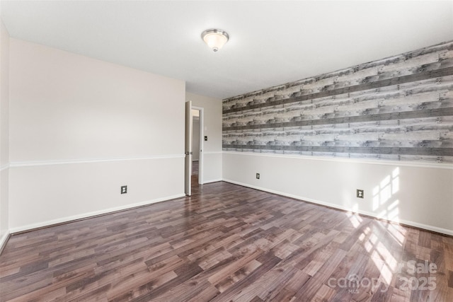 empty room featuring an accent wall, wood finished floors, and baseboards