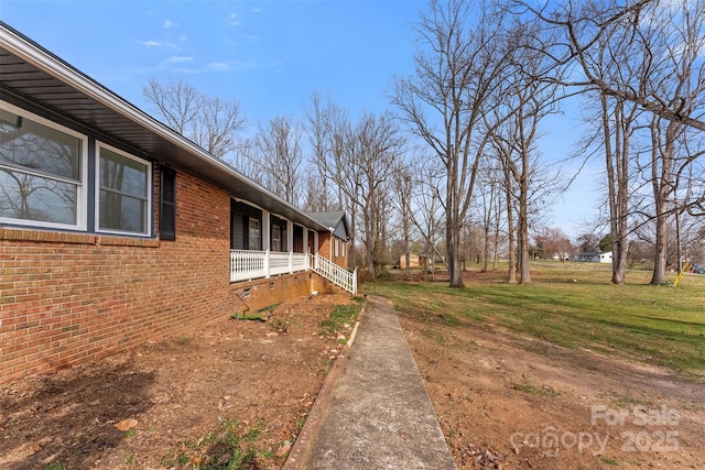 view of side of home featuring brick siding, covered porch, and a yard