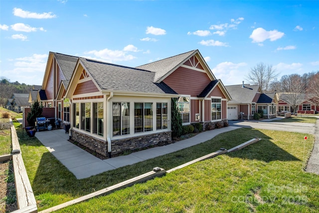 view of front of property with a front lawn, roof with shingles, a garage, a sunroom, and stone siding