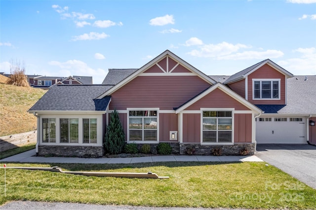 craftsman house with a front yard, roof with shingles, a garage, stone siding, and driveway