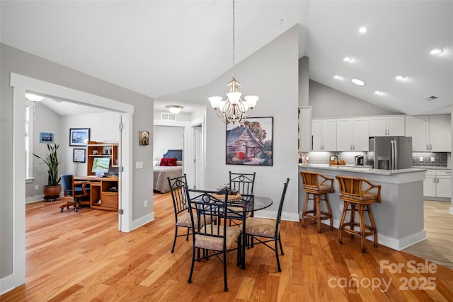 dining room featuring a notable chandelier, visible vents, light wood-type flooring, and high vaulted ceiling