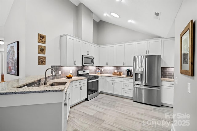 kitchen featuring light stone countertops, a peninsula, a sink, stainless steel appliances, and white cabinets