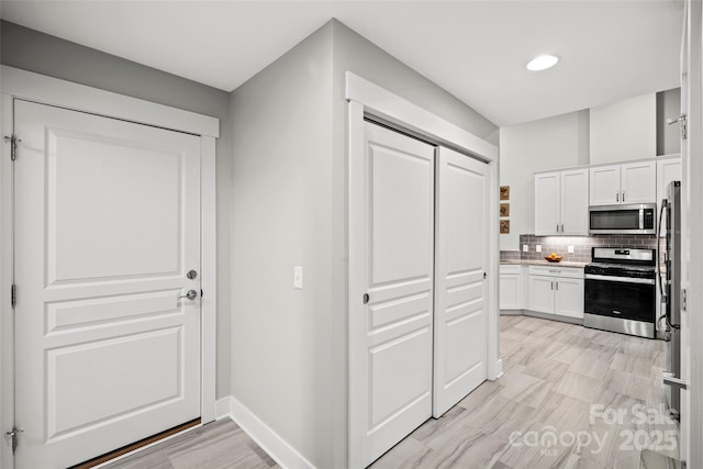 kitchen with baseboards, stainless steel appliances, light countertops, white cabinetry, and backsplash