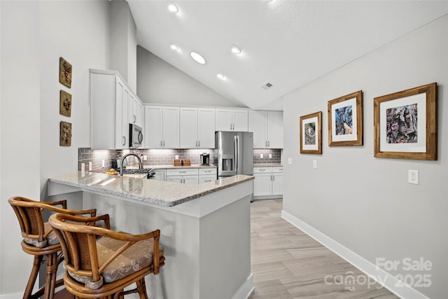 kitchen with tasteful backsplash, light stone countertops, a kitchen bar, a peninsula, and stainless steel appliances