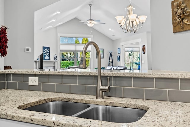 kitchen with ceiling fan with notable chandelier, lofted ceiling, light stone countertops, and a sink