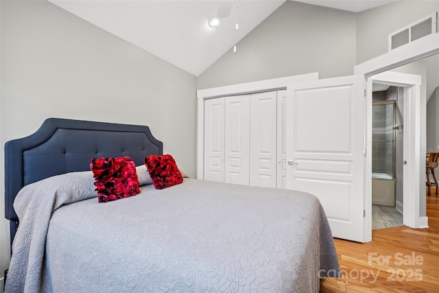 bedroom with a closet, visible vents, high vaulted ceiling, and light wood-style floors