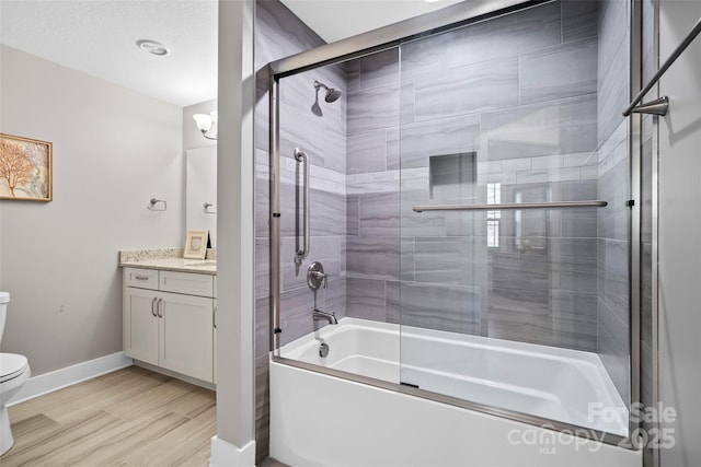 bathroom with vanity, wood finished floors, baseboards, toilet, and combined bath / shower with glass door