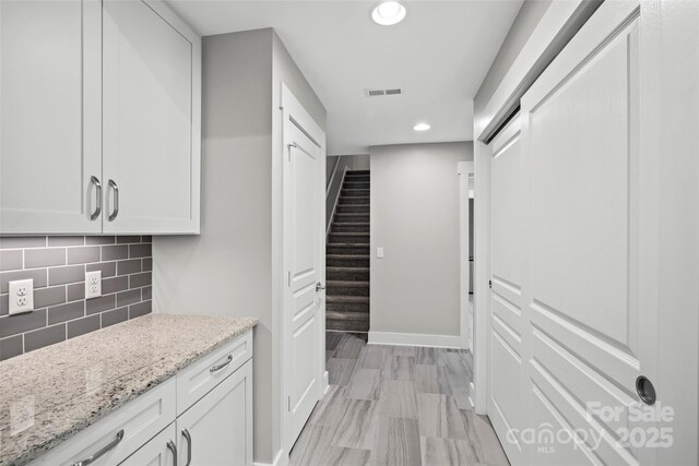 interior space with visible vents, baseboards, light stone countertops, decorative backsplash, and recessed lighting