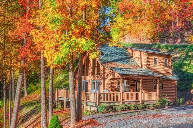 log-style house with log siding, covered porch, and metal roof