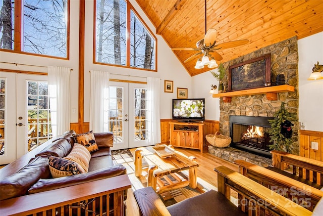 living room with a stone fireplace, wainscoting, french doors, wooden ceiling, and wood finished floors