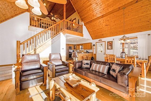 living room featuring stairway, light wood-style flooring, wooden ceiling, ceiling fan with notable chandelier, and high vaulted ceiling