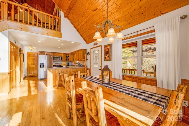 dining area featuring light wood-type flooring, a wainscoted wall, high vaulted ceiling, wood ceiling, and a chandelier