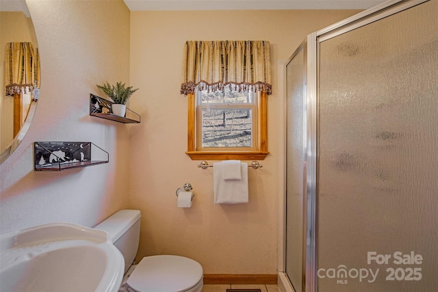 bathroom with a stall shower, toilet, baseboards, and a sink