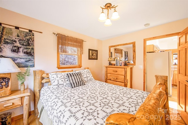 bedroom featuring light wood finished floors, a chandelier, and freestanding refrigerator