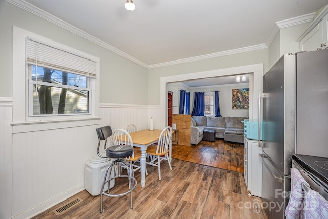 dining room featuring visible vents, ornamental molding, a wainscoted wall, and wood finished floors