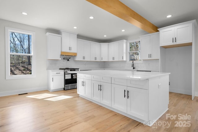 kitchen with beam ceiling, light wood-style flooring, white cabinetry, gas range, and baseboards