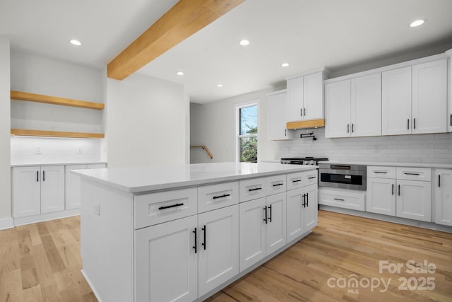 kitchen with beam ceiling, light wood finished floors, open shelves, a kitchen island, and light countertops