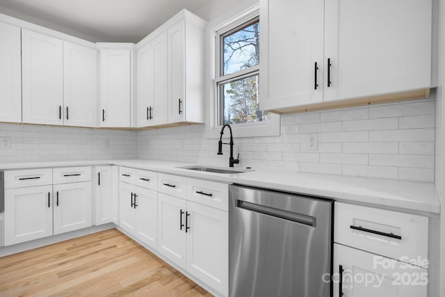 kitchen featuring light wood finished floors, a sink, decorative backsplash, and stainless steel dishwasher