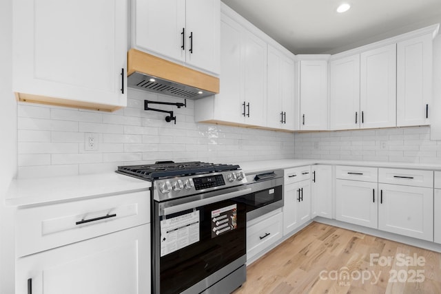 kitchen with decorative backsplash, light countertops, white cabinets, gas range, and light wood-type flooring