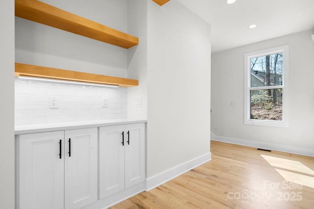 interior space featuring baseboards, light wood finished floors, open shelves, decorative backsplash, and white cabinets