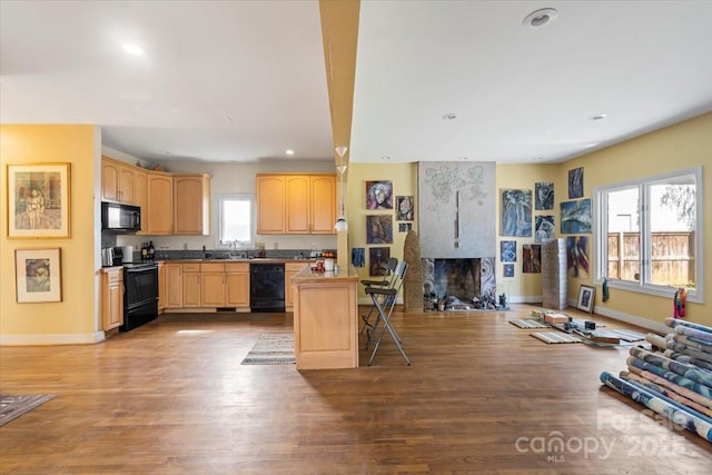 kitchen featuring wood finished floors, black appliances, a fireplace, and light brown cabinetry