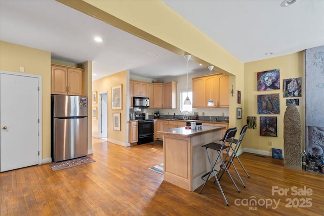 kitchen featuring black appliances, light wood-style flooring, a breakfast bar area, and a sink