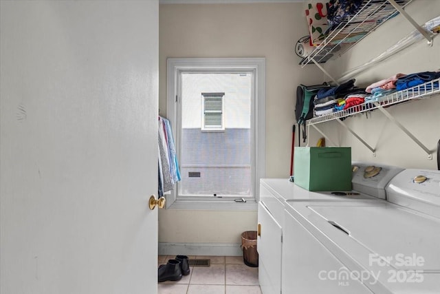 clothes washing area with laundry area, light tile patterned floors, washing machine and dryer, and baseboards