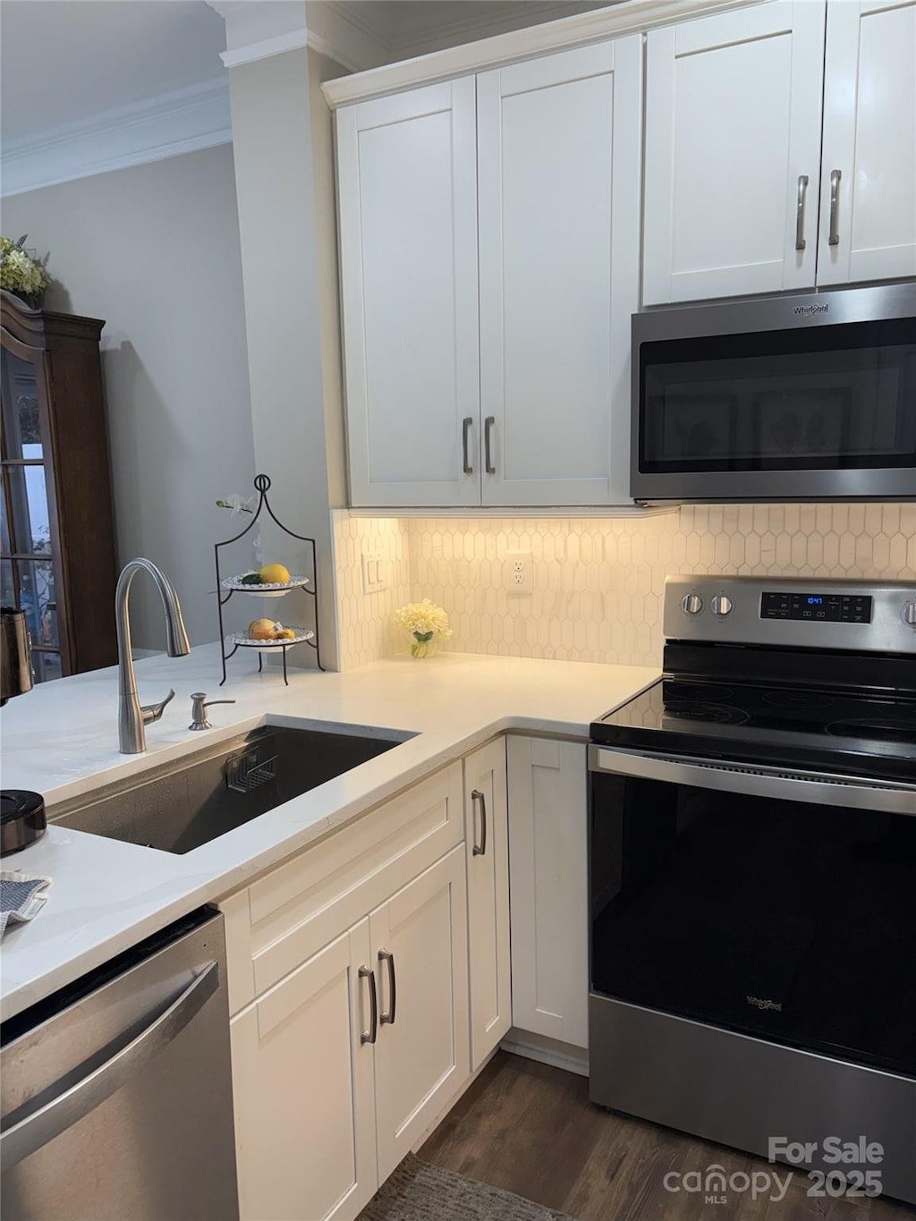 kitchen featuring ornamental molding, decorative backsplash, light countertops, a sink, and appliances with stainless steel finishes