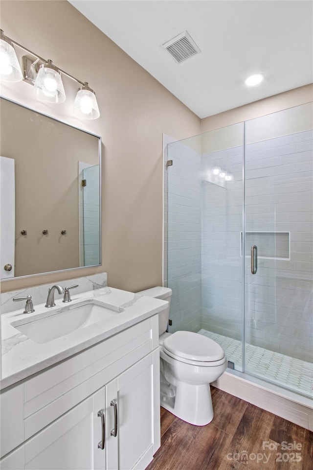 bathroom with visible vents, a shower stall, toilet, wood finished floors, and vanity