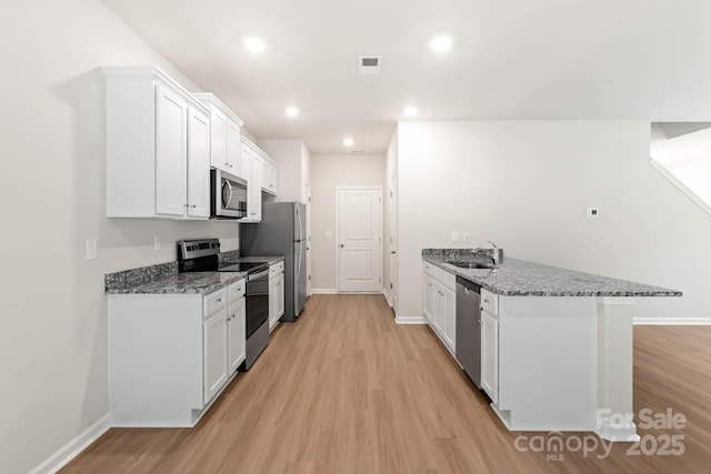 kitchen with a peninsula, stainless steel appliances, light wood-style floors, white cabinetry, and a sink