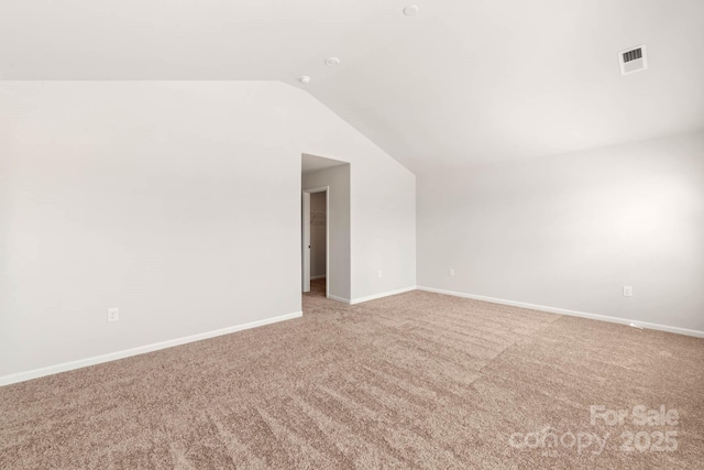 carpeted empty room featuring visible vents, baseboards, and lofted ceiling