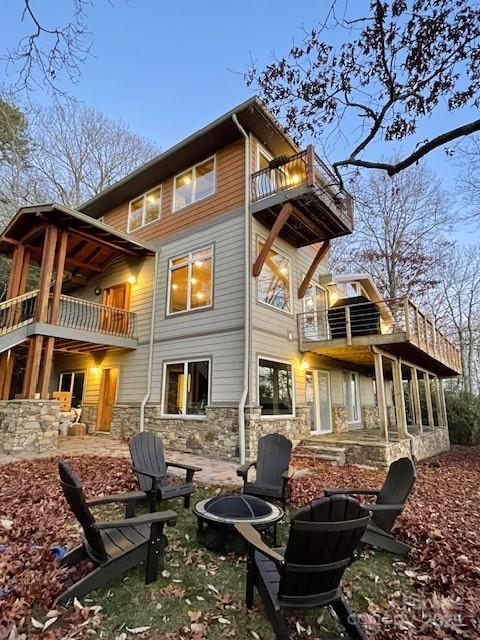 back of property featuring a patio area, stone siding, a fire pit, and a balcony