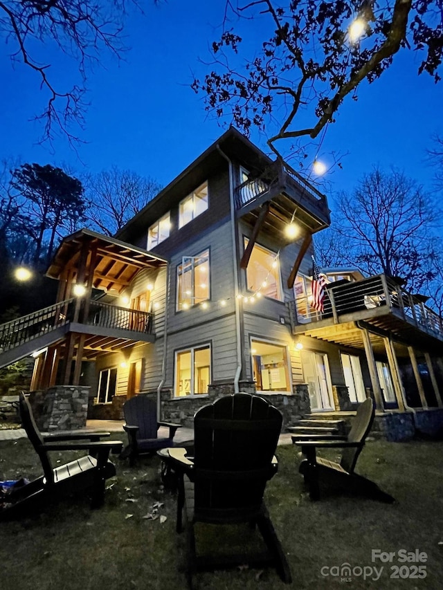 back of house at night with a balcony and stone siding